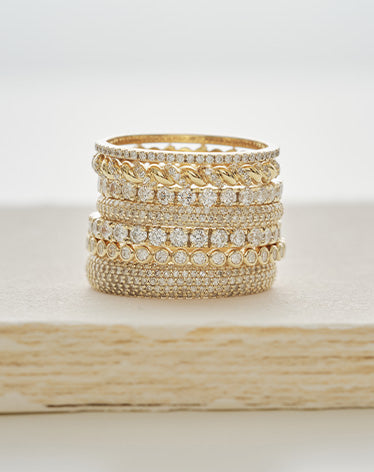 Stack of gold and diamond rings on a light wooden surface
