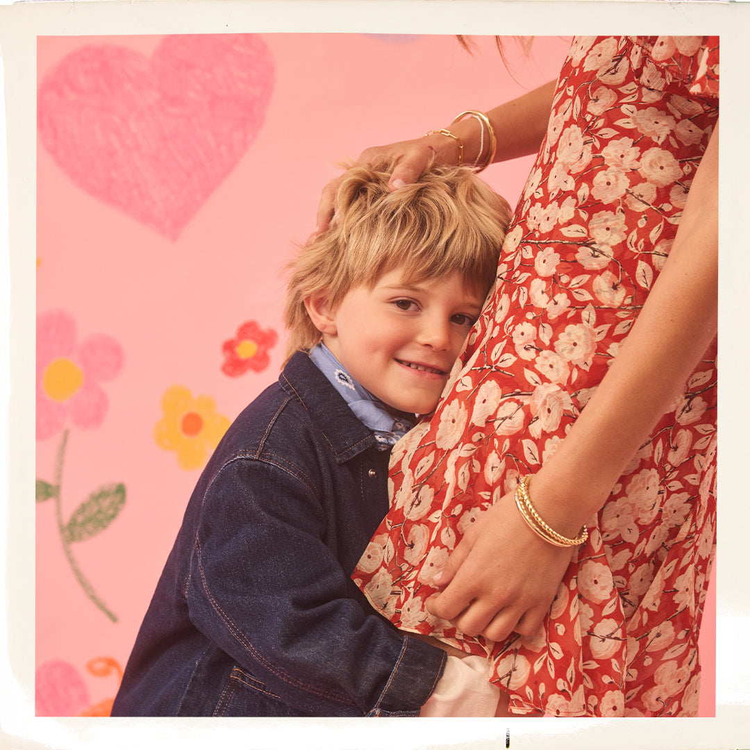 Child in denim jacket with adult in floral dress against a pink background with hearts and flowers