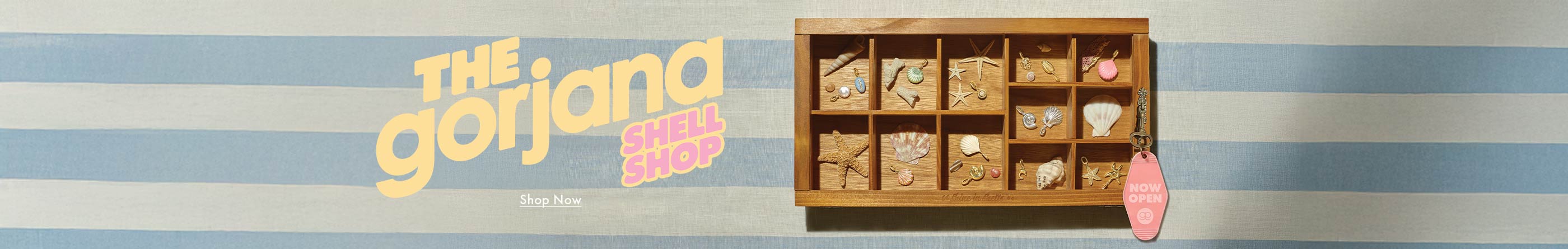Wooden jewelry box with shell jewelry on a striped background, featuring 'The Gorjana Shell Shop' branding.
