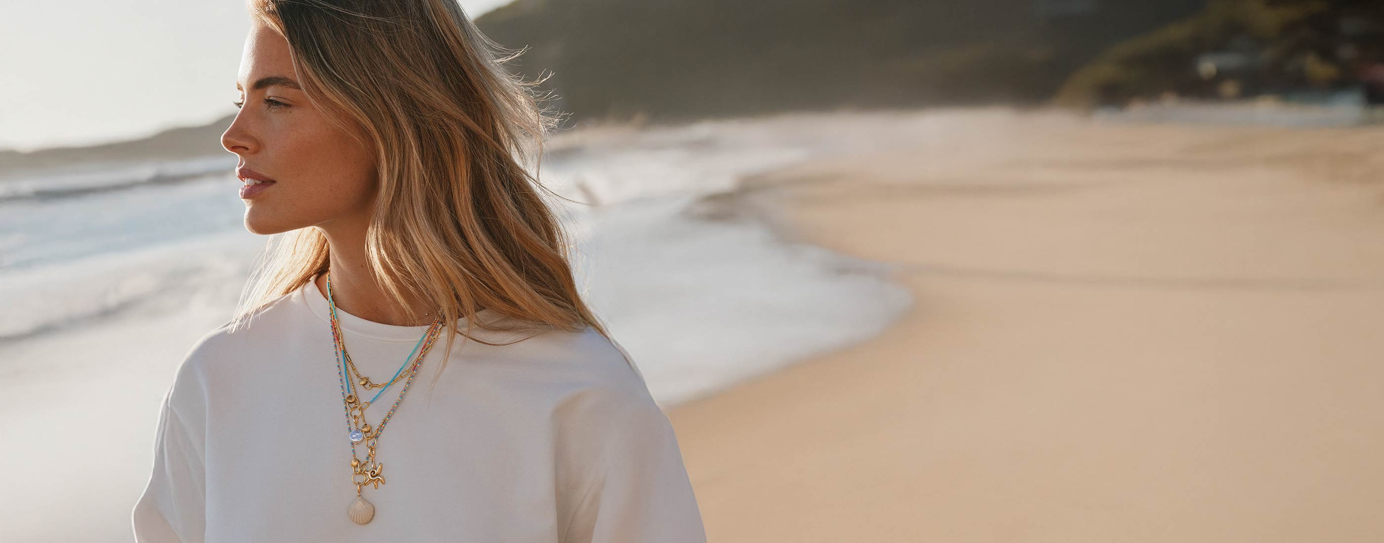 Woman on the beach, wearing layered necklaces and charms 