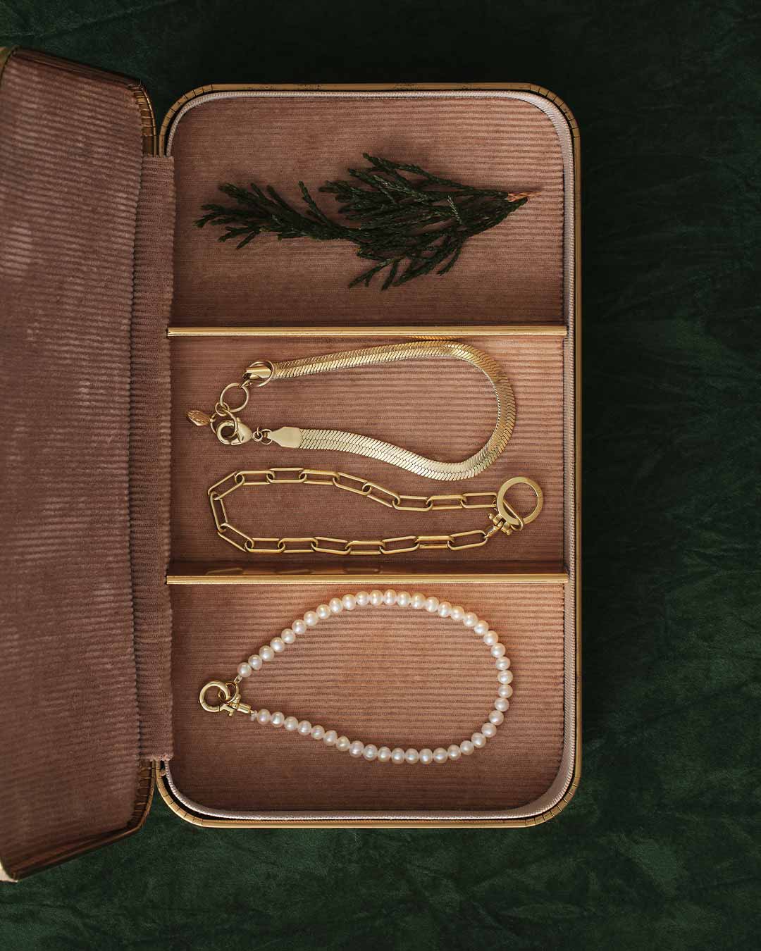 Jewelry set including a gold chain and pearl necklace displayed in an open brown jewelry box.