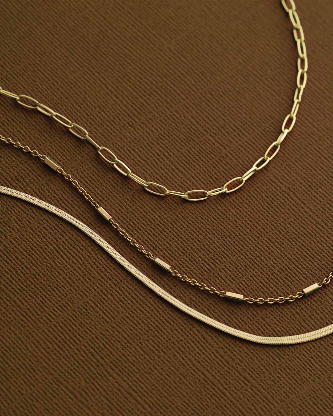 Two gold chains on a brown textured surface