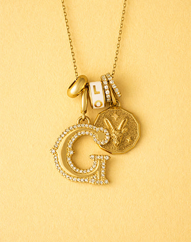 Gold necklace with letter 'G' pendant on a yellow background