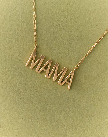 Gold 'MAMA' necklace on a green background
