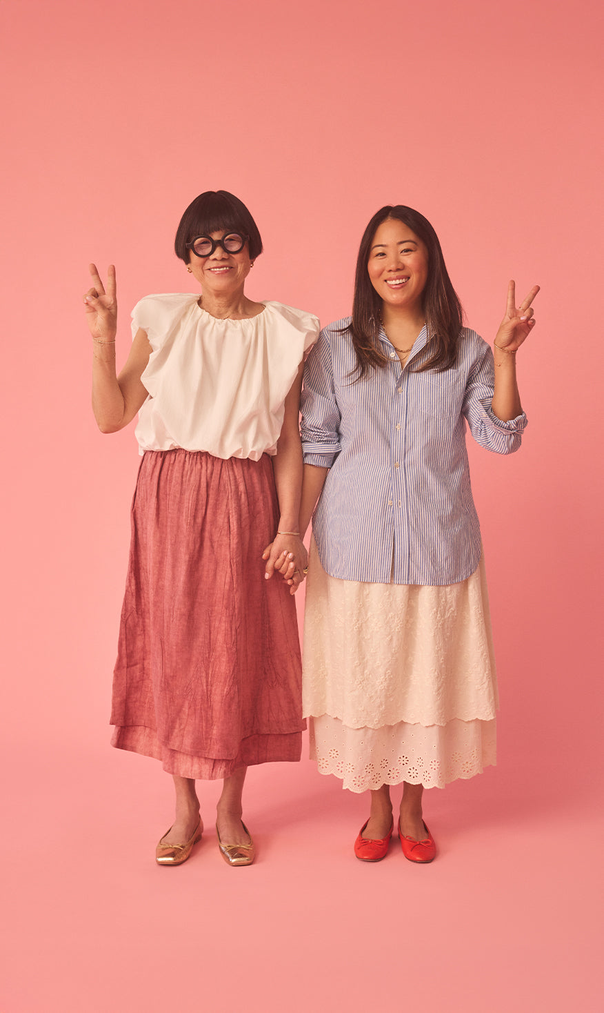 Aki & Yuri posing against a pink background, wearing colorful outfits.